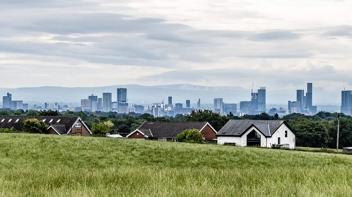 The Manchester skyline in the distance beyond green fields and houses