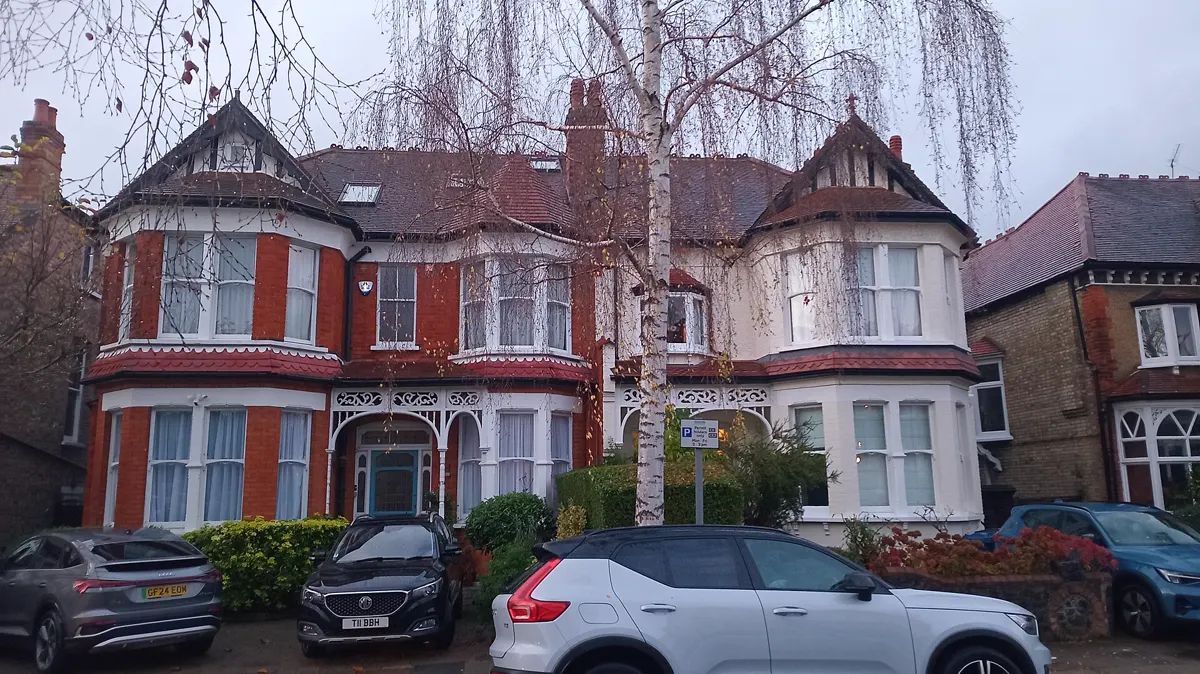 A pair of large semi-detached red-brick houses with cars parked outside