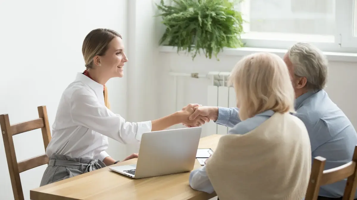 An adviser shaking hands with an older couple across a kitchen table