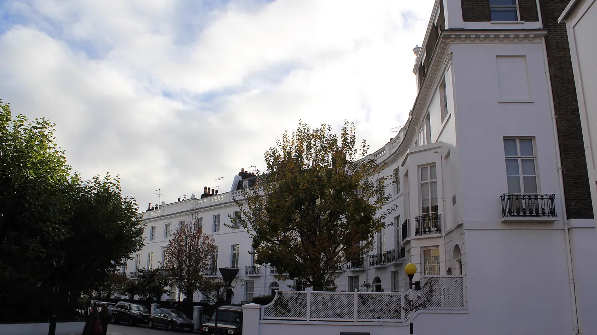 A curved terrace of white stucco houses at Pelham Place in London under a cloudy sky